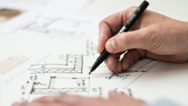Close-up of hand drawing intricate technical designs on blueprint with pen, ideal for engineering or architecture themes.
